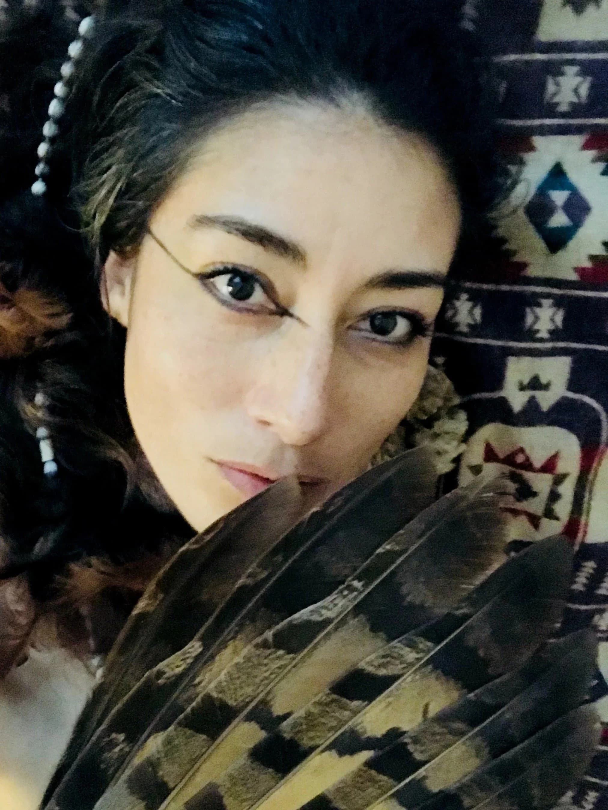 Portrait of Ximena Xaguar, her face half hidden behind a fan of hawk feathers
