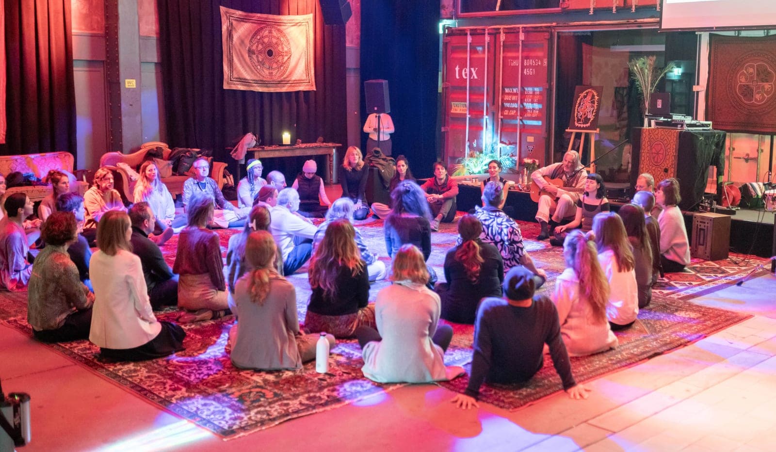 Participants seated on carpets in a hall during a Re Evolution Art gathering