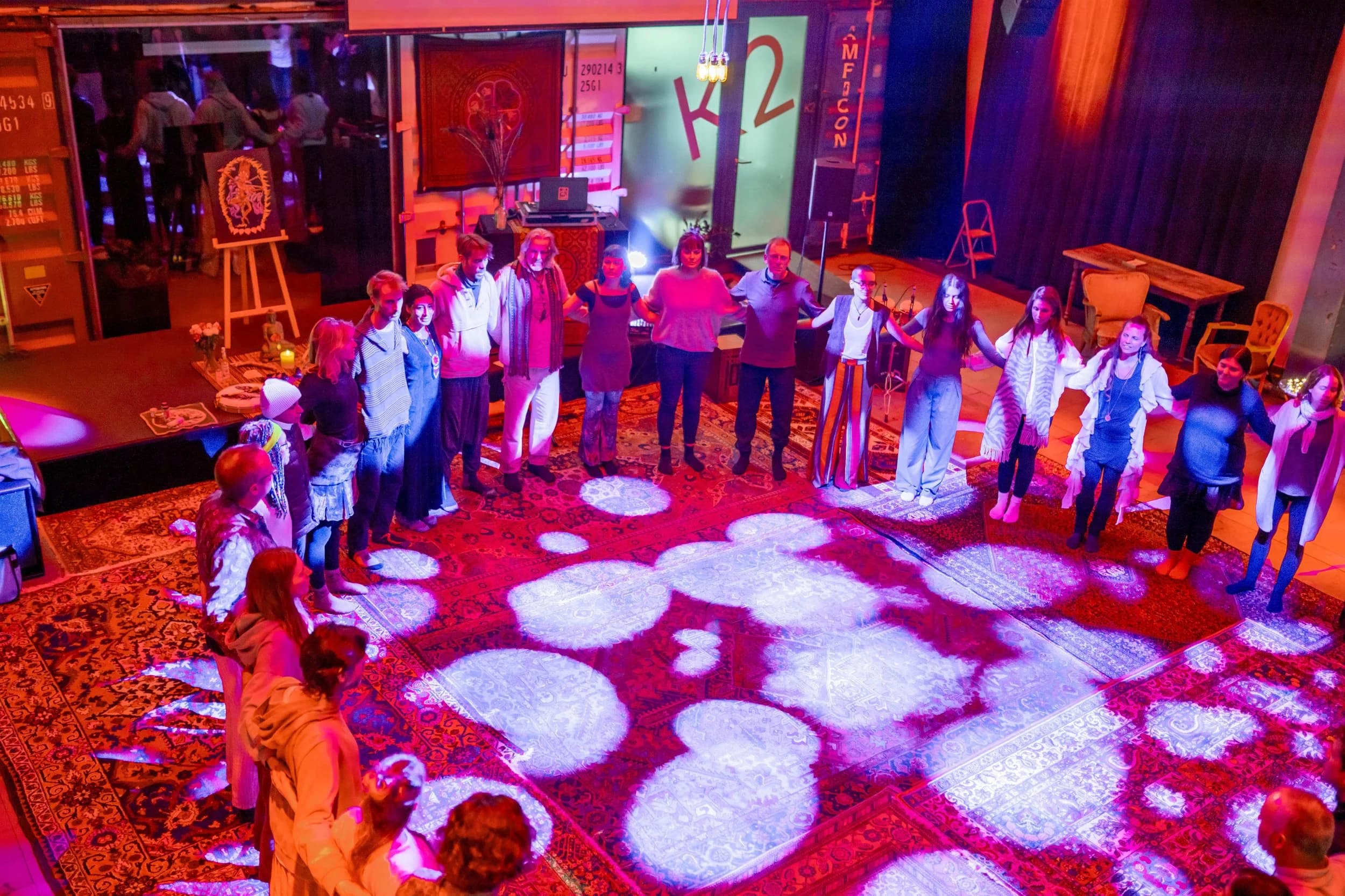 A circle of participants holding hands on a carpeted stage lit in purple